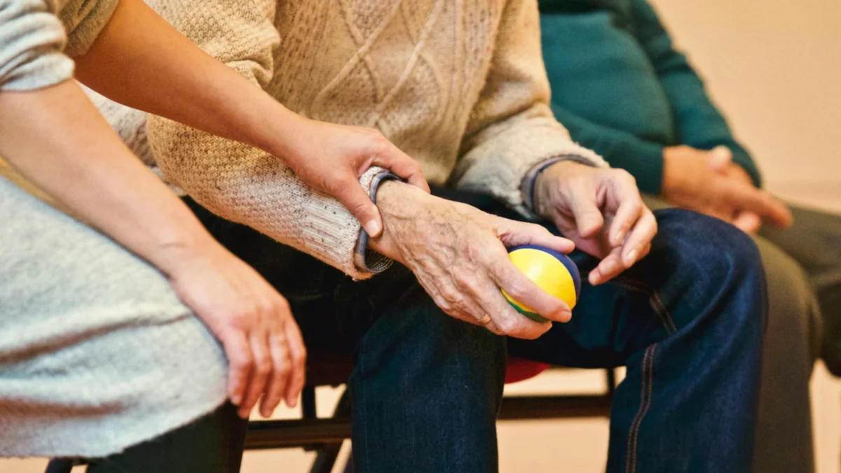 A caregiver's hand gently resting on an elderly person's arm in a comforting gesture